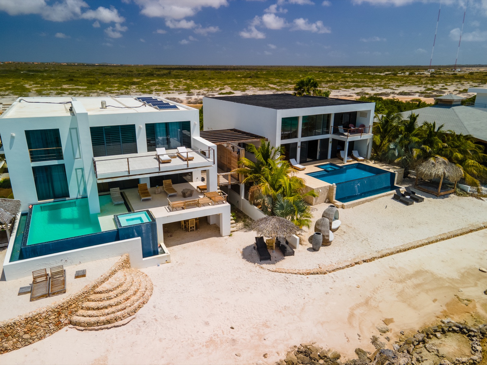 Aerial view of a luxury Bonaire villa with modern white architecture, two private infinity pools, and direct sandy beach access on the Caribbean coast.